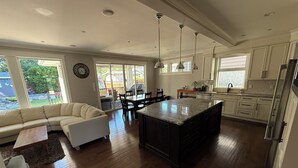 Eine moderne Küche mit einer zentralen Kochinsel, einem Essbereich mit Stühlen und einem Wohnzimmer mit einer Couch.