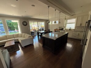 A modern kitchen with a central island, dining area with chairs, and a living room with a sofa.