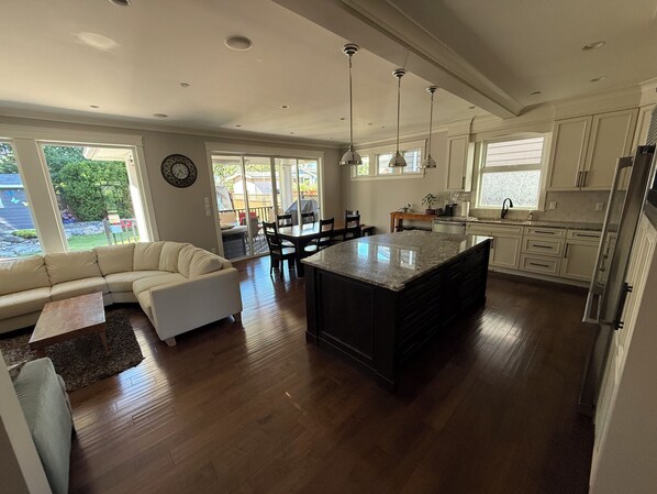 A modern kitchen with a central island, dining area with chairs, and a living room with a sofa.