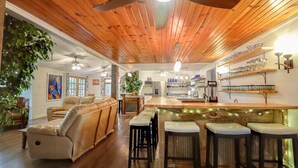 A cozy living room with a wooden ceiling, a sofa, and a bar area with stools. - Beautiful golf course getaway on Madeline island<br> (La Pointe)