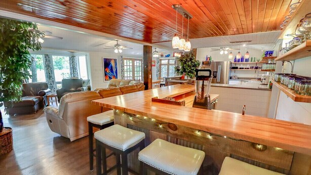 A spacious living room with a wooden ceiling, a large island bar with stools, and a kitchen area visible in the background. - Beautiful golf course getaway on Madeline island<br> (La Pointe)