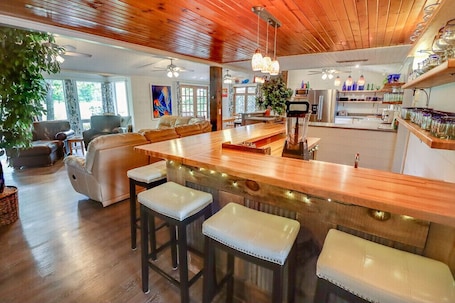 A spacious living room with a wooden ceiling, a large island bar with stools, and a kitchen area visible in the background.