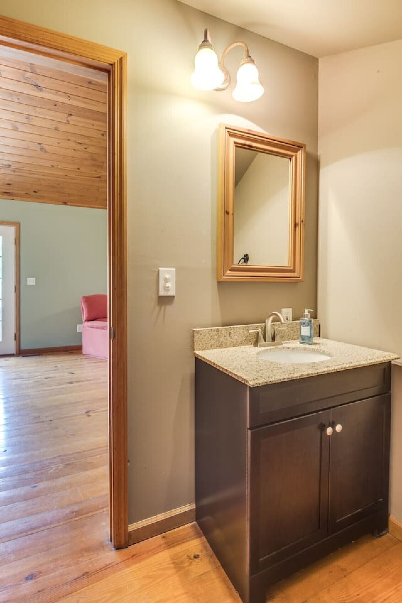 Un baño con tocador de madera oscura, encimera de color claro y espejo montado en la pared.