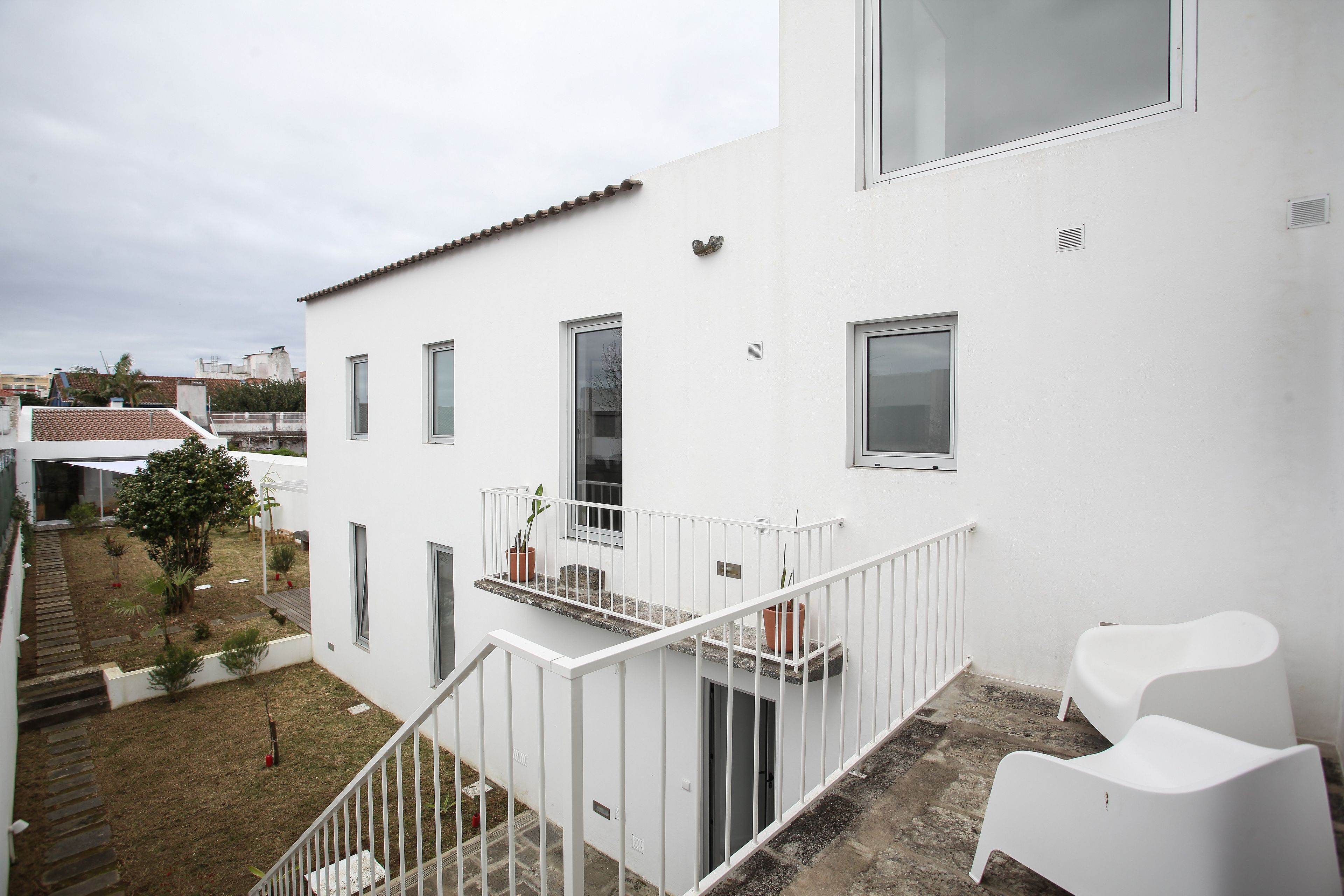 Un bâtiment moderne de couleur blanche, doté d’un balcon, d’un petit jardin et d’un escalier menant à l’entrée.