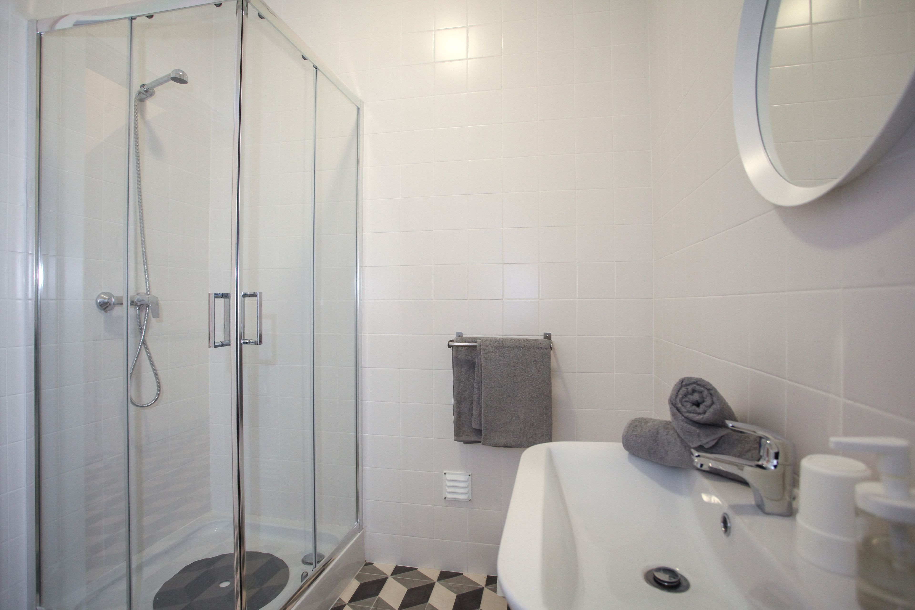 Un bagno con doccia vetro, lavandino con specchio e porta asciugamani.