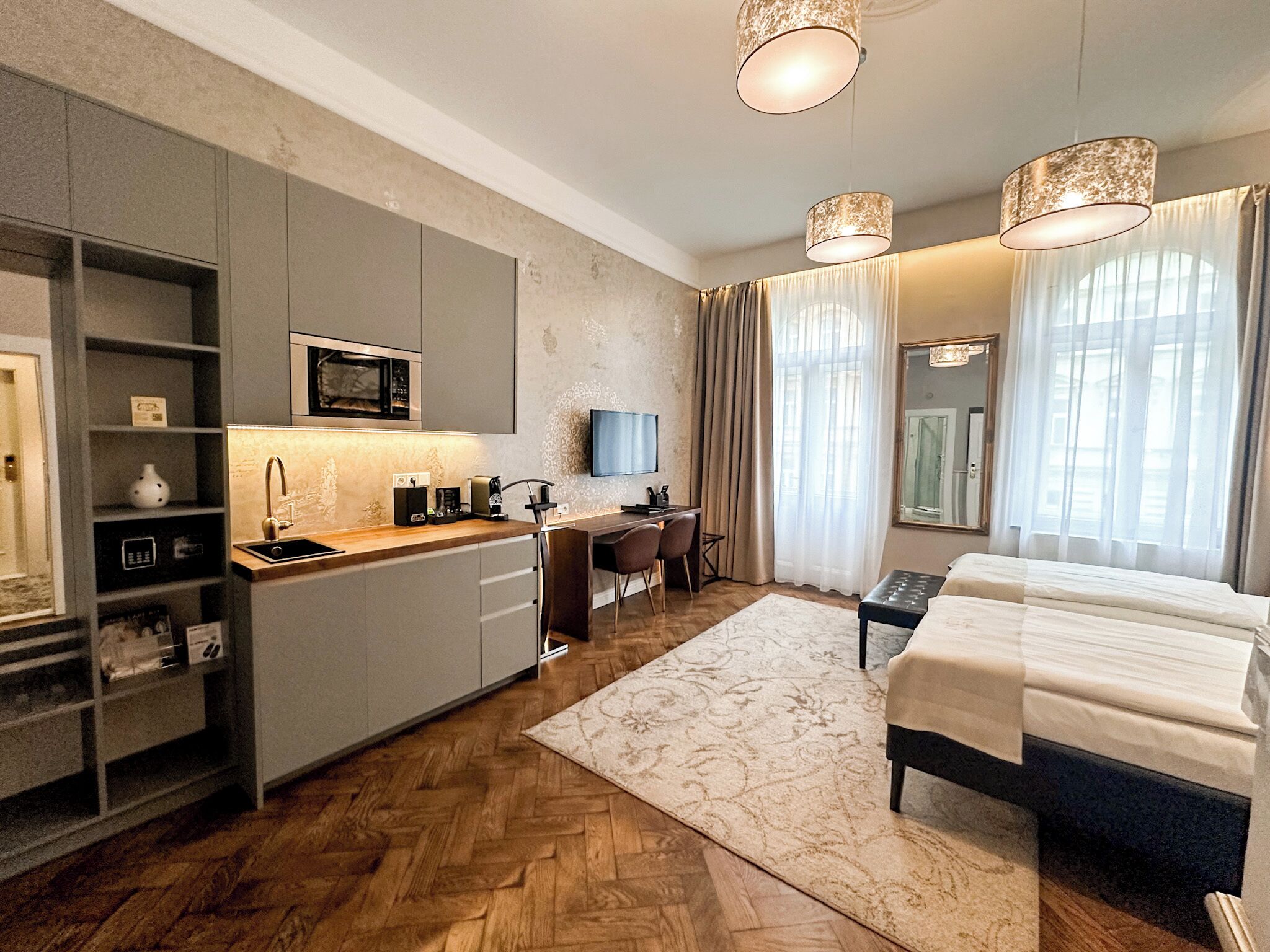 A modern hotel room with a kitchenette, a bed, a desk, and a TV.