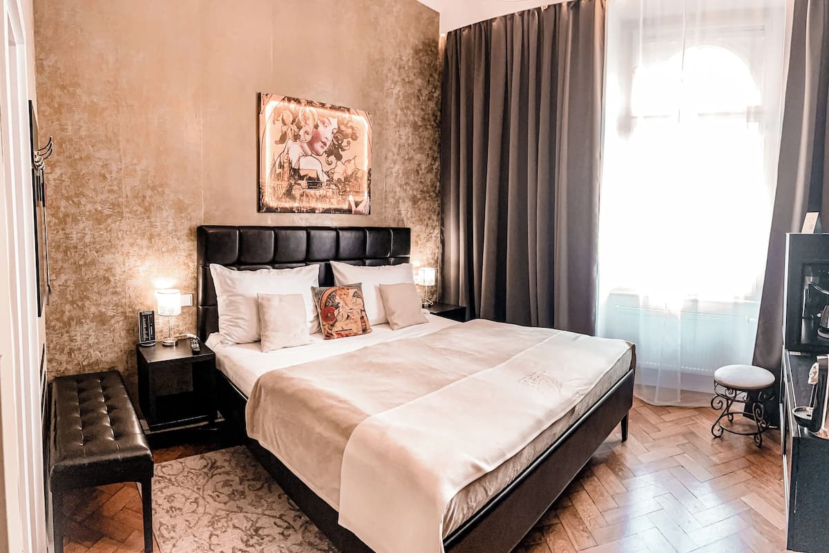 A neatly arranged bedroom with a large bed, a bedside table with a lamp, a bench, and a painting on the wall.