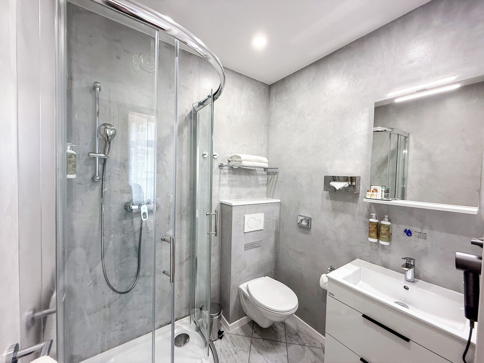 Un baño moderno con ducha de vidrio, inodoro, lavabo y espejo.