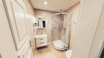 Un baño con ducha de mampara de vidrio, un lavamanos blanco y un espejo encima.