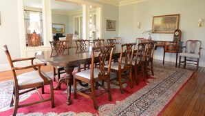 A dining room with a large wooden table surrounded by chairs, a patterned rug, and a painting on the wall.