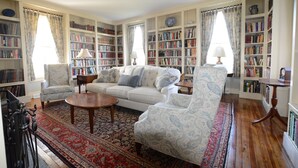 A spacious living room with a large bookshelf, a sofa, armchairs, and a coffee table.