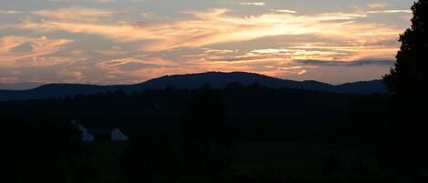 Un coucher de soleil sur un paysage vallonné, avec une maison au premier plan.