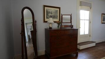 A room with a wooden dresser, a mirror, a framed picture on the wall, and a door with a window.