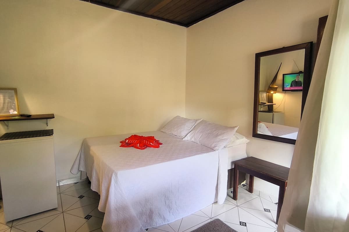 Quarto de hotel com cama, mesa de cabeceira, espelho e televisão.