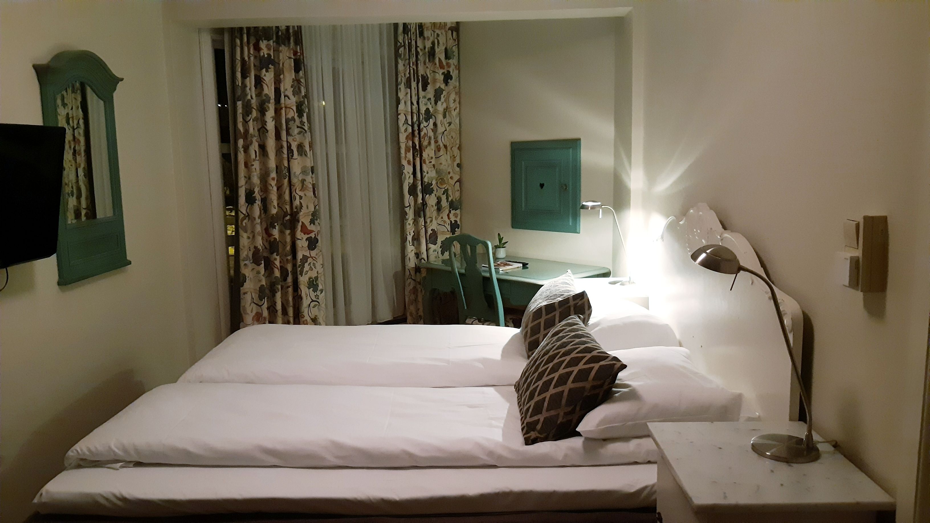 Een hotelkamer met een bed, bureau, stoel, lamp en gordijnen.