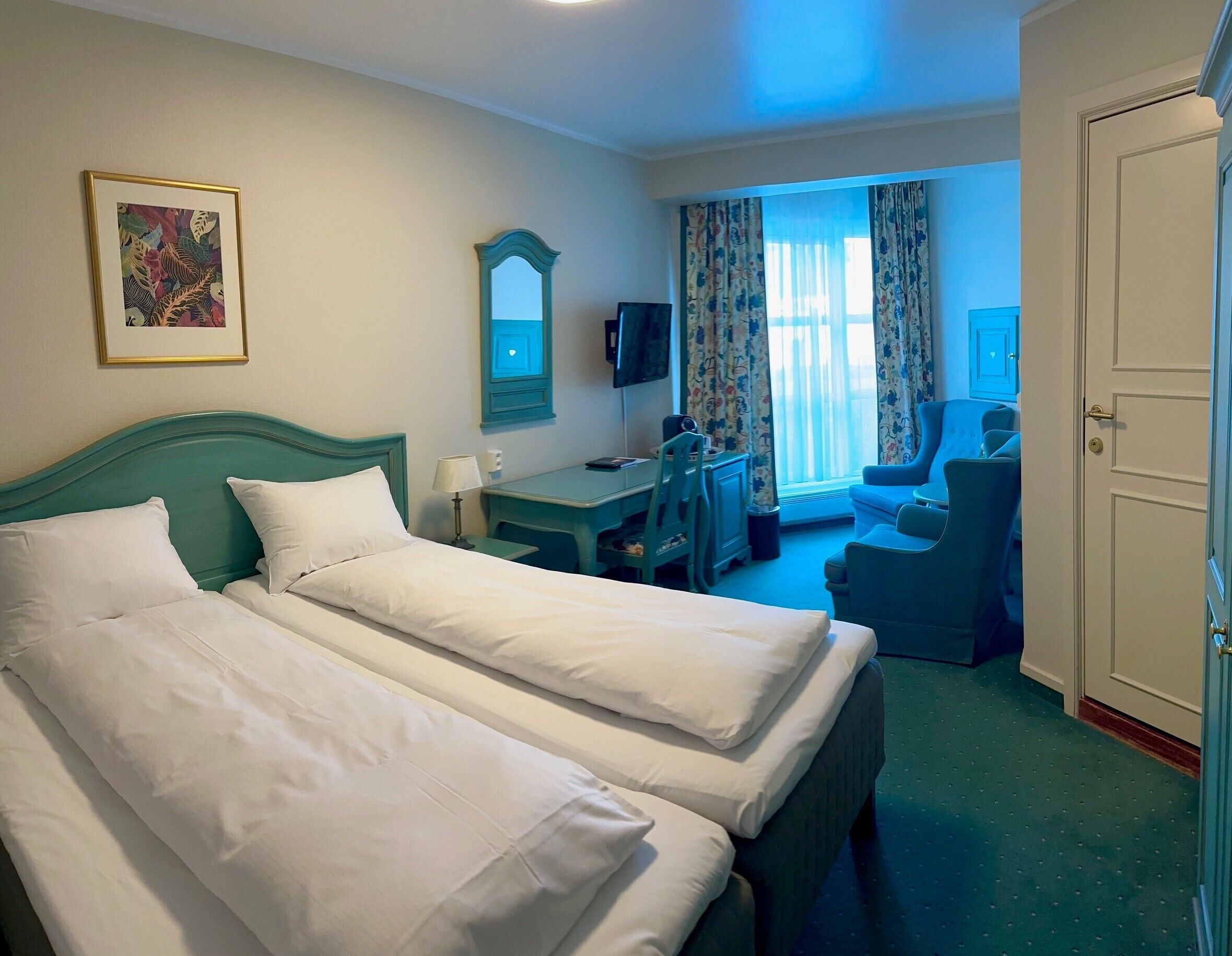 Una habitación de hotel con dos camas, un escritorio, una silla, un televisor y una puerta.