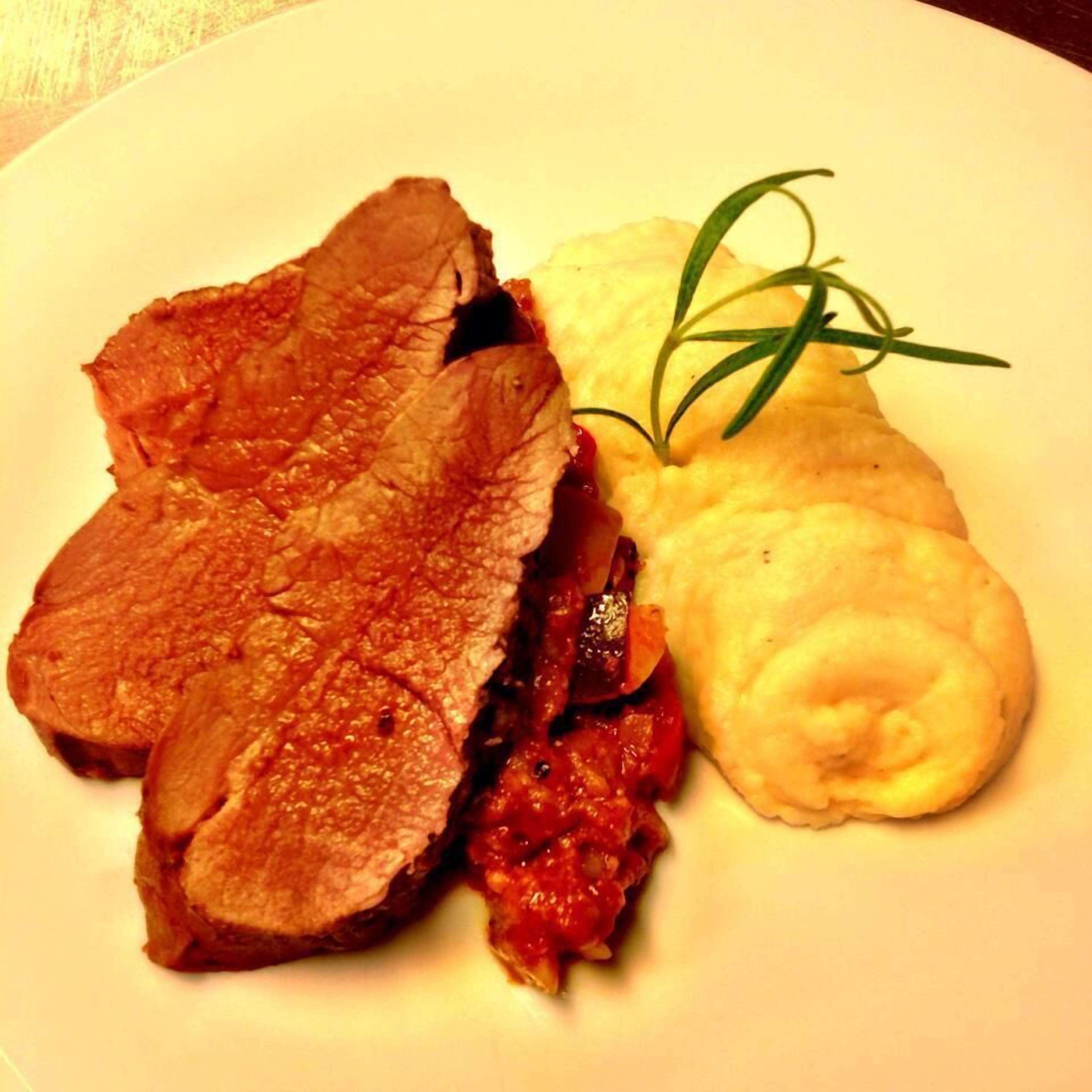 Ein Teller mit geschnittenem Braten, Tomatensauce und Kartoffelpüree.