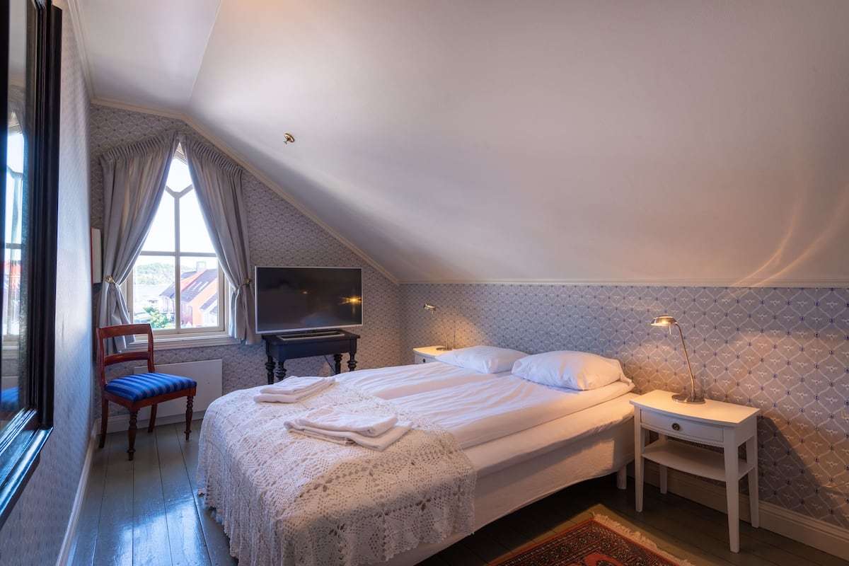 Un dormitorio con una cama grande, una silla, un televisor y una mesita de noche con lámpara.
