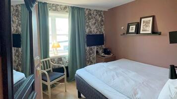 A hotel room with a bed, a chair, a desk, a lamp, and a window with curtains.