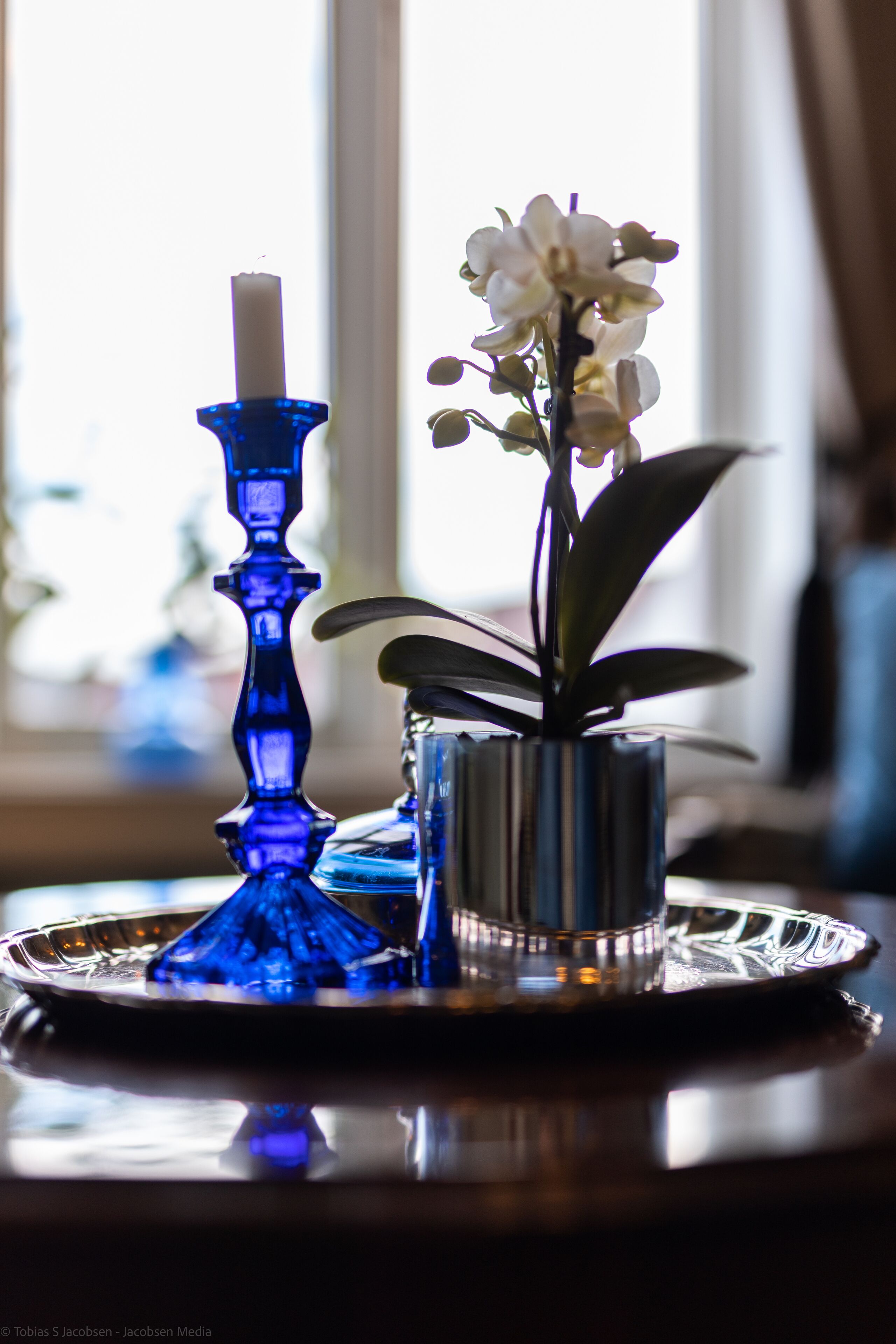A blue candle holder with a white candle and a small potted orchid on a reflective tray.