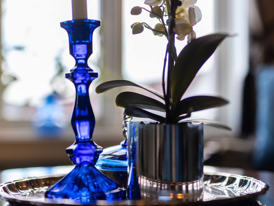A blue candle holder with a white candle and a small potted orchid on a reflective tray.