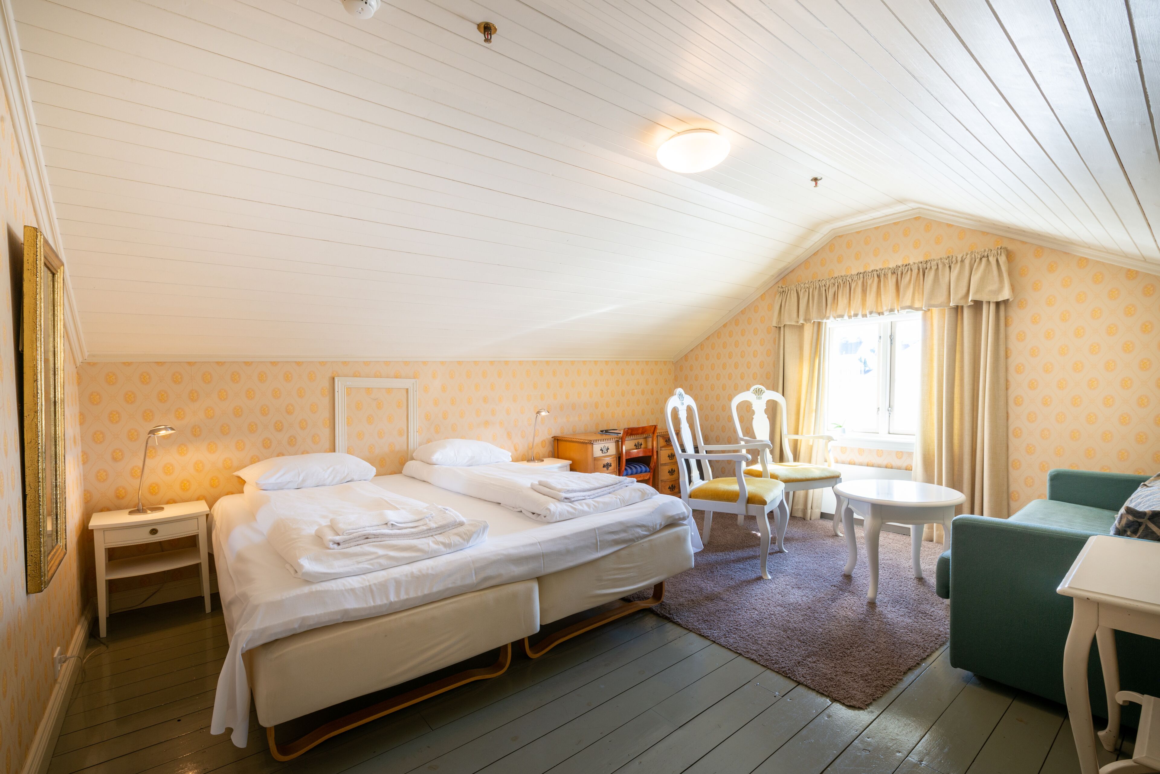 A bedroom with two beds, a small table, a chair, and a window with curtains.