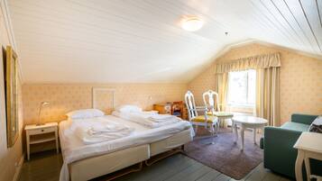 A bedroom with two beds, a small table, a chair, and a window with curtains.