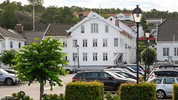 A white building with a traditional architectural style, a parking area with cars, and a street lamp.