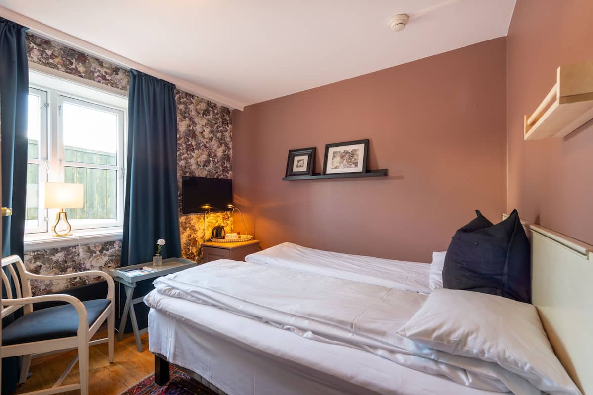 Habitación de hotel con cama, escritorio, silla y ventana con cortinas.