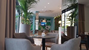 A modern lounge area with comfortable seating, a large TV screen, and decorative plants.
