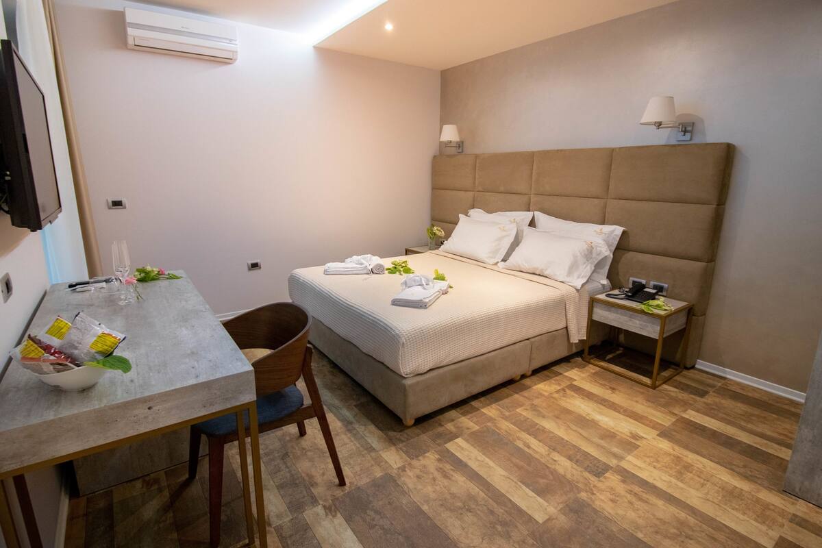 A bedroom with a bed, bedside table, chair, and a small table with items on it.