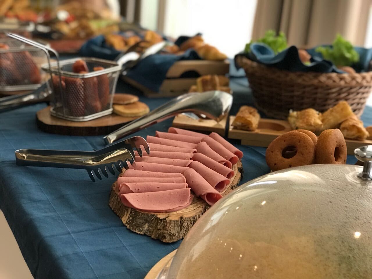 Een buffettafel met plakjes ham, een tang en een mand met gebak.