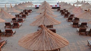 A beach with rows of wooden lounge chairs and thatched umbrellas.