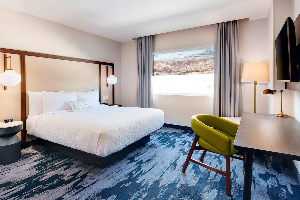 A hotel room with a bed, a desk, a chair, a TV, and a window with a view.
