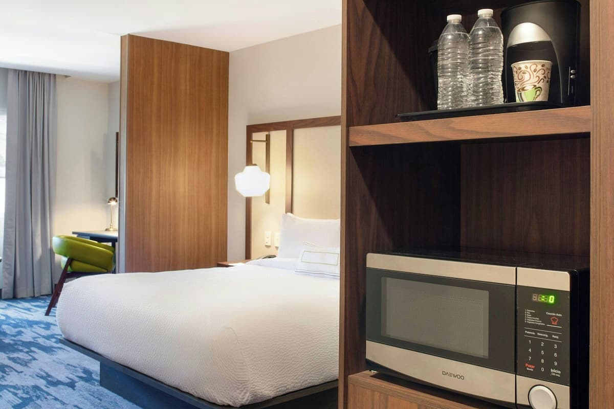A hotel room with a bed, a microwave, a refrigerator, and a shelf with water bottles and a coffee maker.