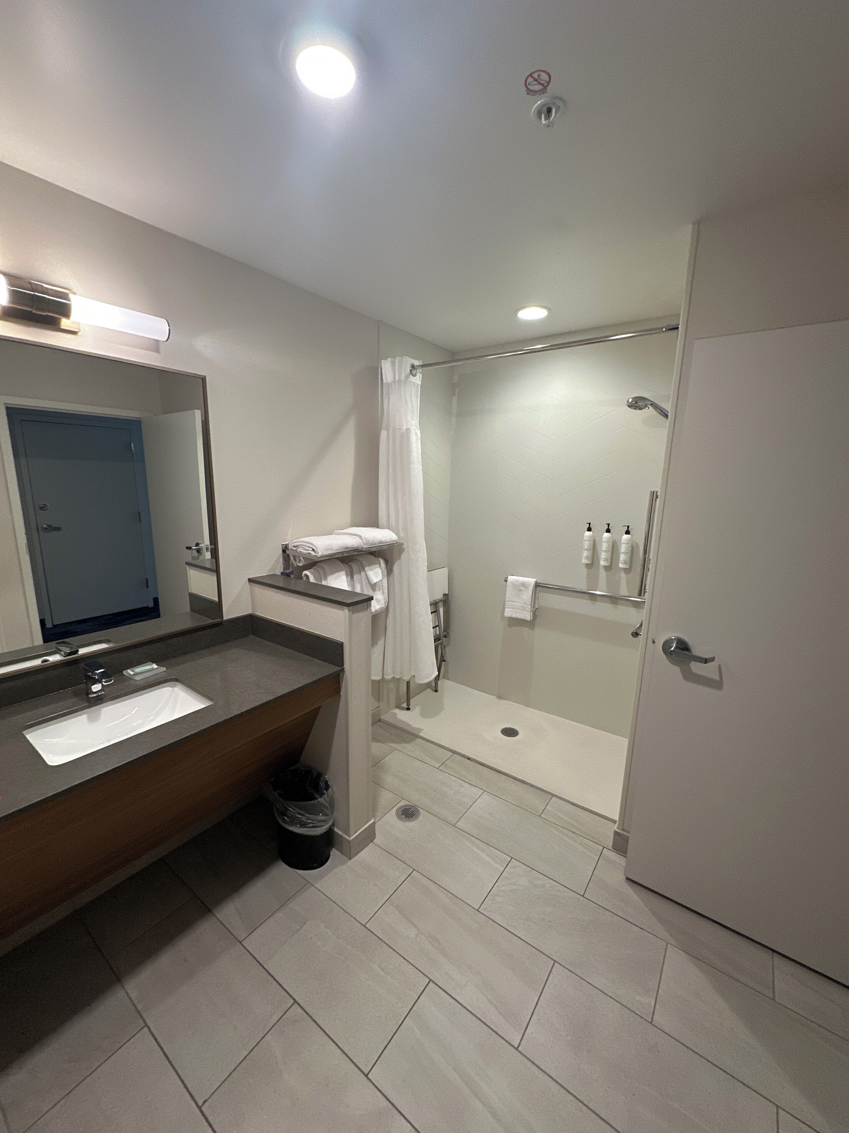 Un baño moderno con lavamanos, espejo, ducha e inodoro.