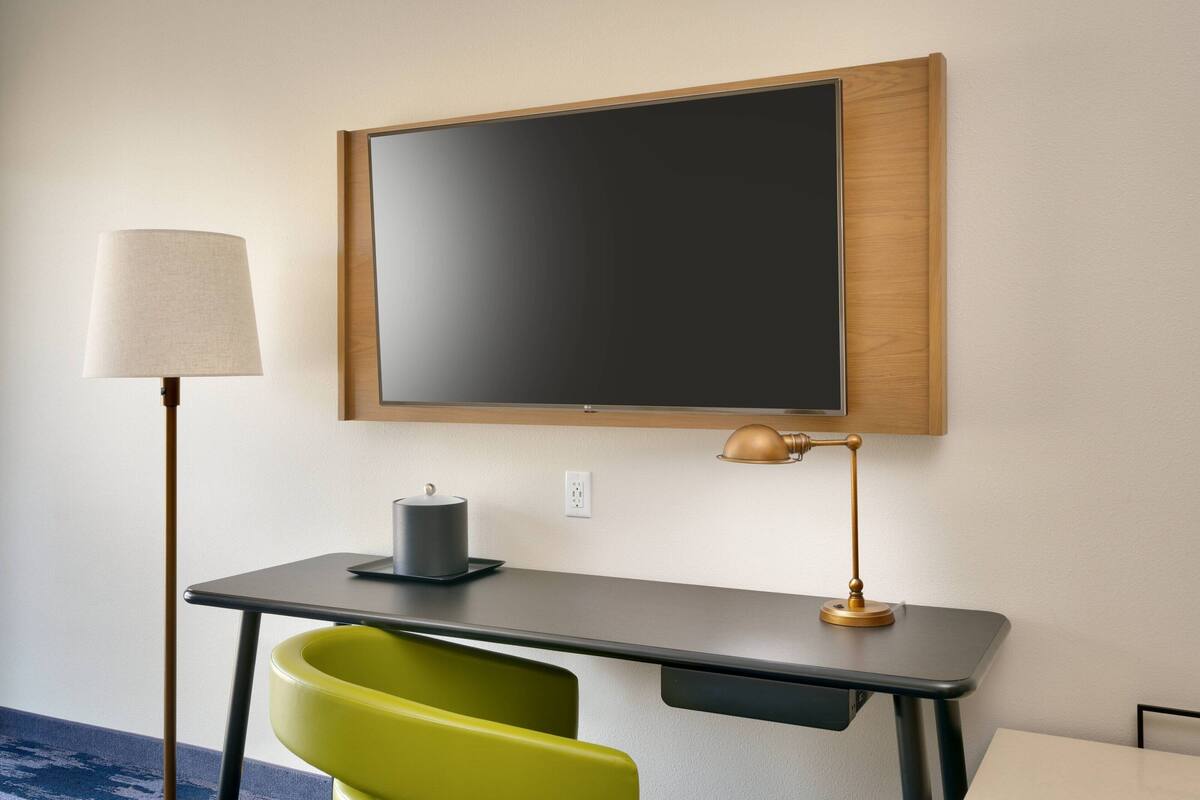 A modern room with a desk, a chair, a lamp, and a television mounted on the wall.