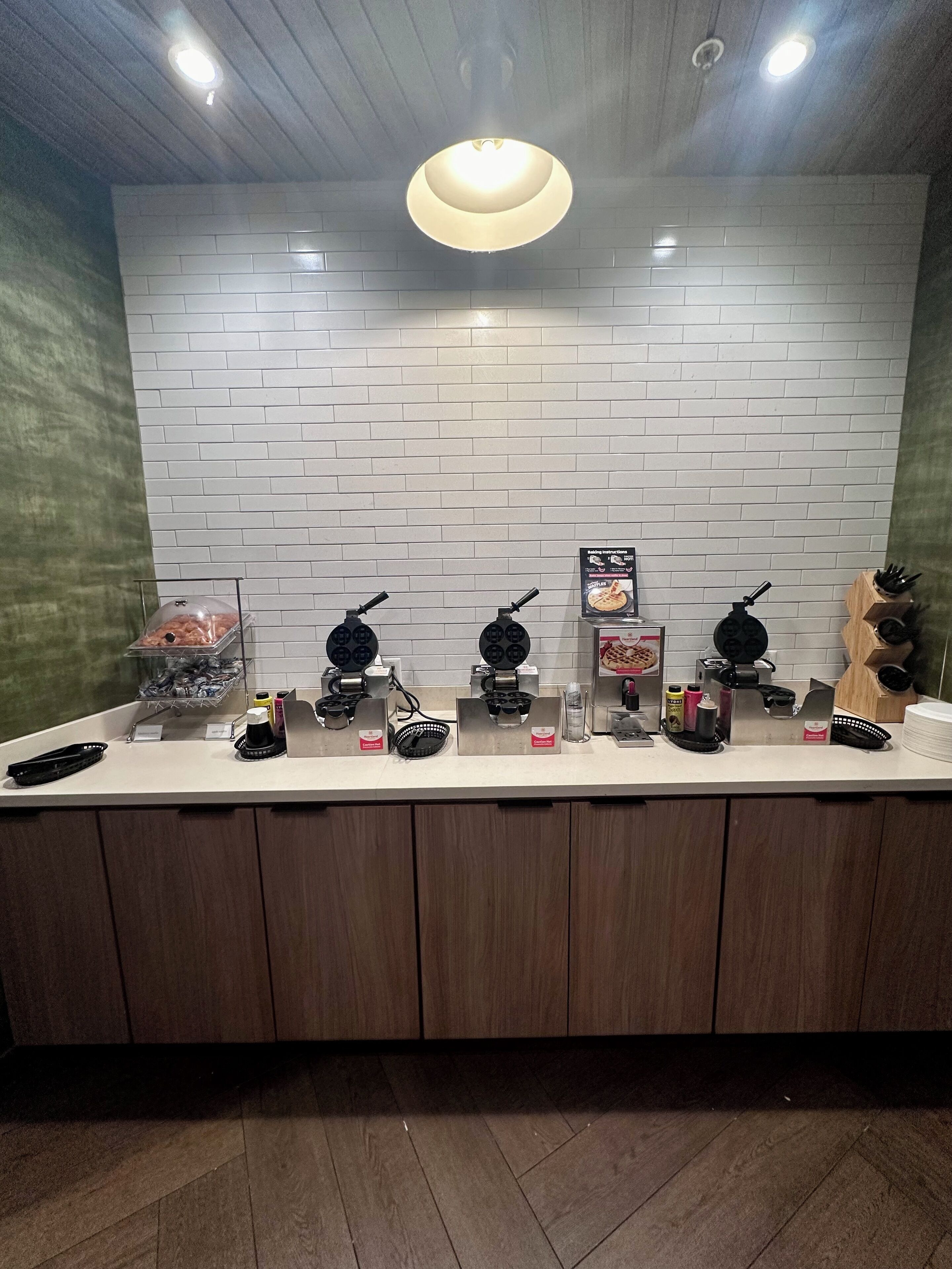 A kitchen counter with various appliances and utensils, a white brick backsplash, and a wooden ceiling.