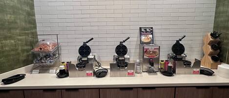 A kitchen counter with various appliances and utensils, a white brick backsplash, and a wooden ceiling.