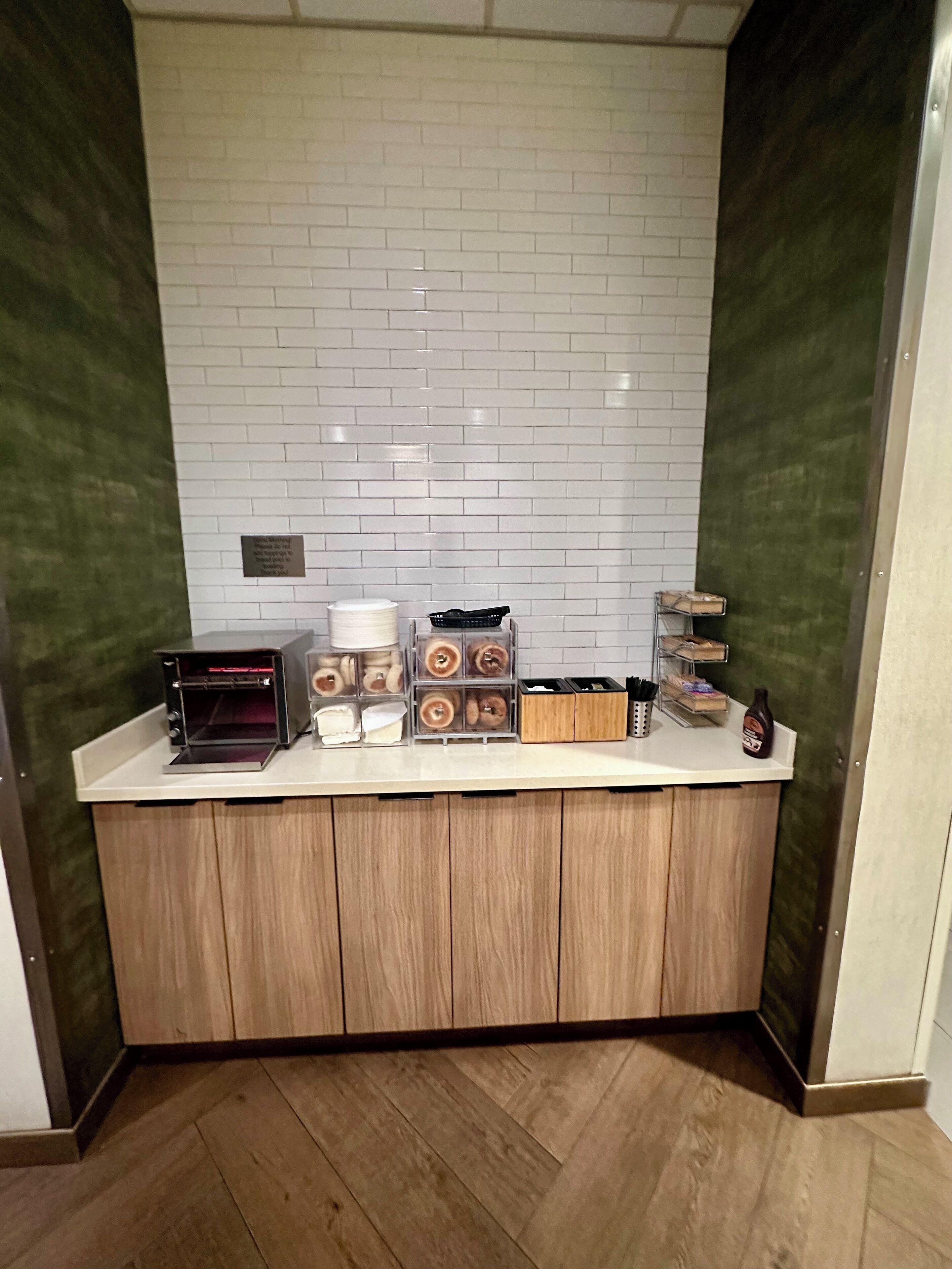 A kitchenette with a white tiled backsplash, a coffee machine, a toaster, and various containers for food storage.