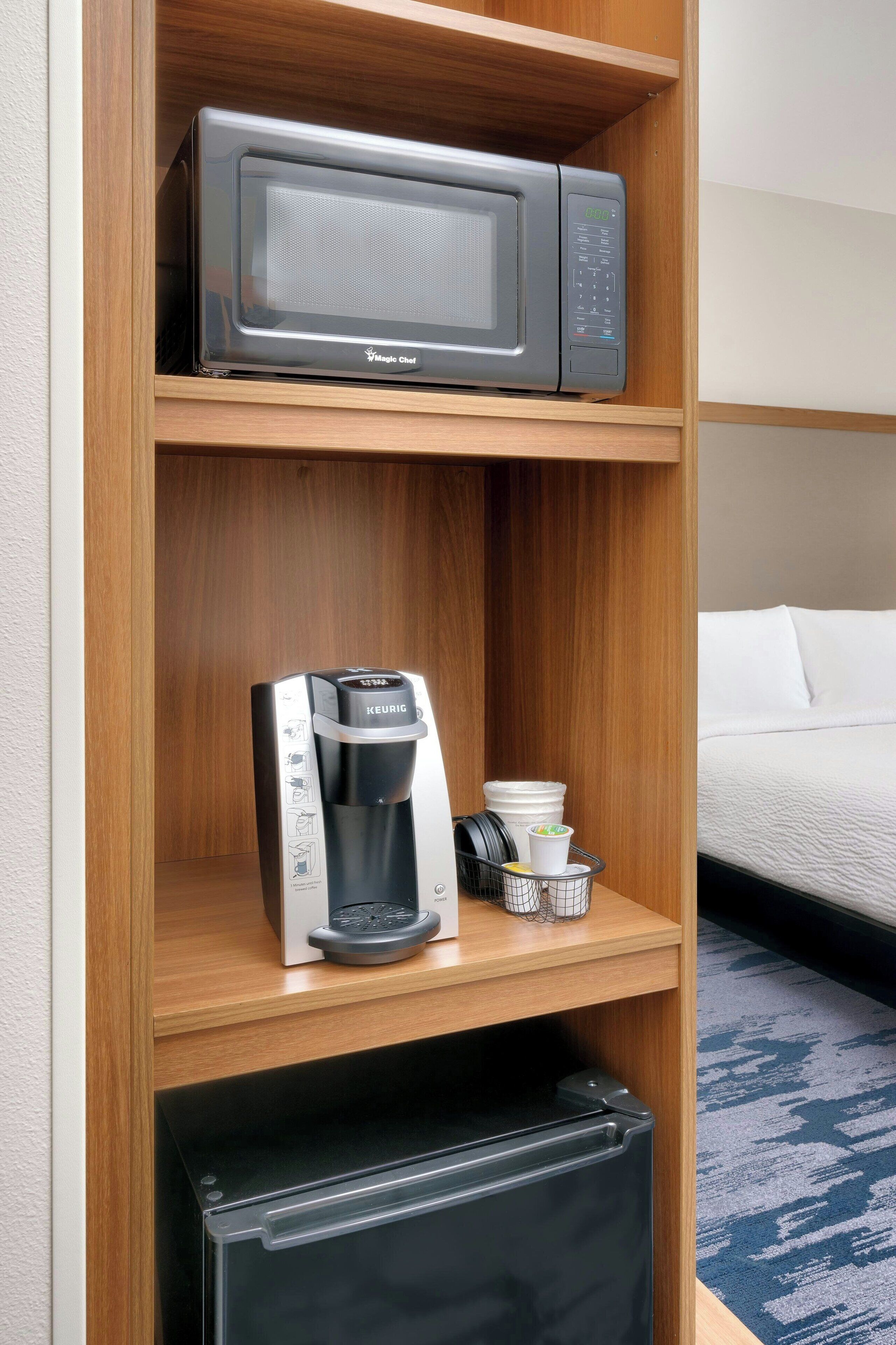 A hotel room with a microwave on the shelf, a coffee maker, and a small refrigerator.