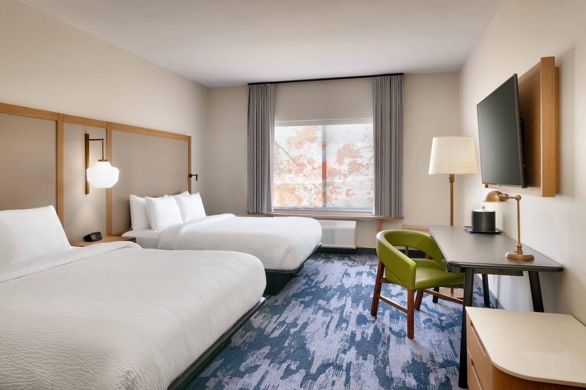 A hotel room with two beds, a desk, a chair, a TV, and a window with curtains.