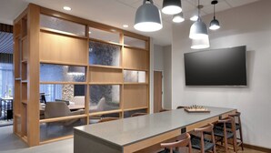 Uma sala de reunião moderna com uma mesa comprida, cadeiras, uma TV e luminárias pendentes.