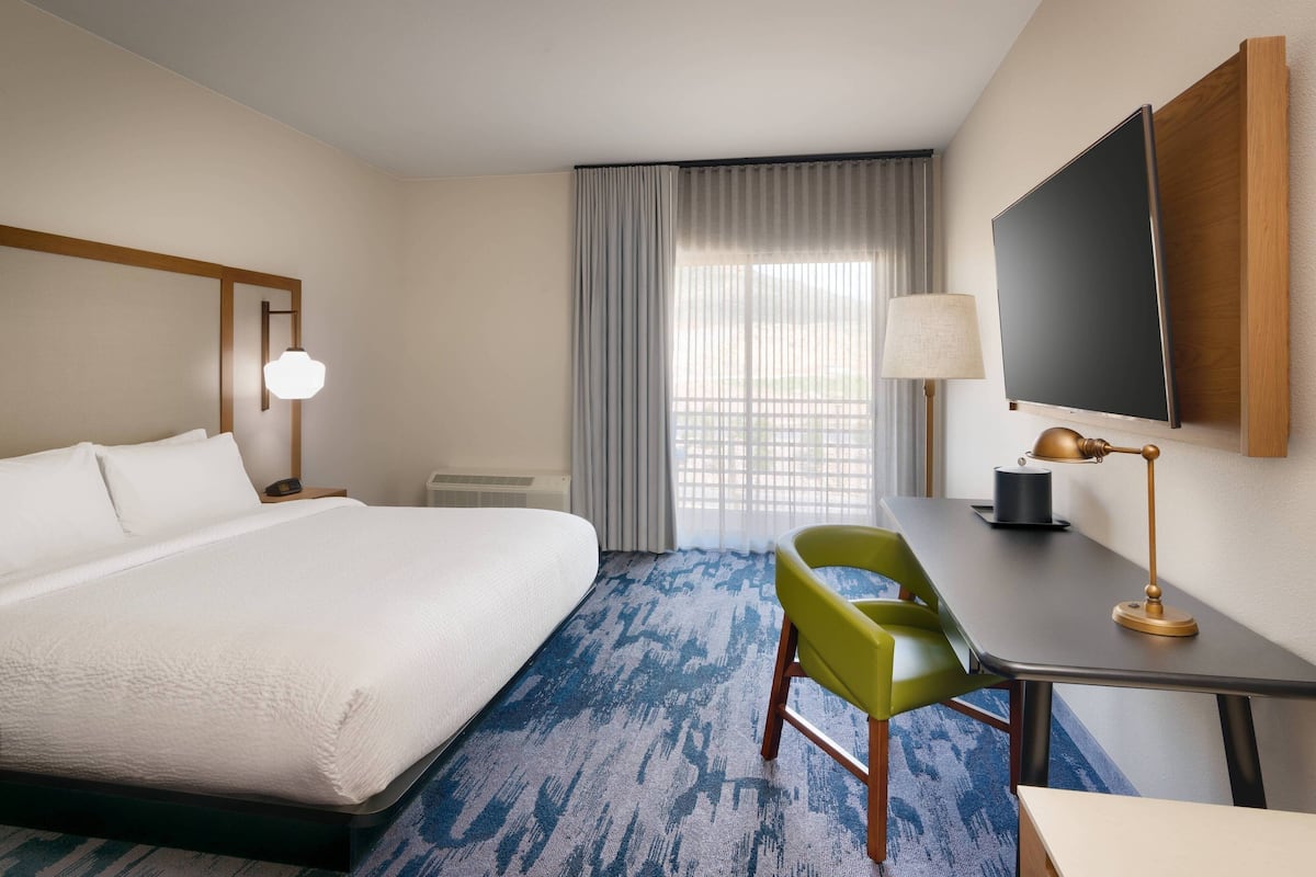 A hotel room with a large bed, a desk with a lamp, a chair, and a TV mounted on the wall.