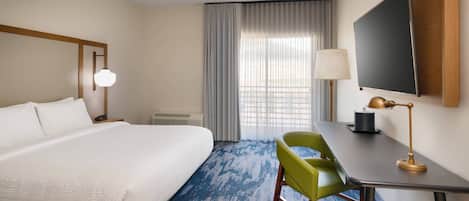 A hotel room with a large bed, a desk with a lamp, a chair, and a TV mounted on the wall.