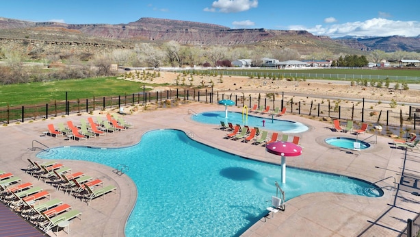 Uma área de piscina com várias piscinas e espreguiçadeiras, cercada por uma grade e com montanhas ao fundo.
