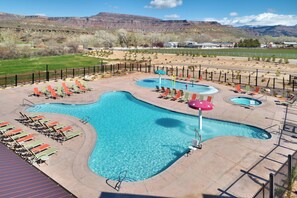 A pool area with multiple pools and lounge chairs, surrounded by a fence and set against a mountainous backdrop.
