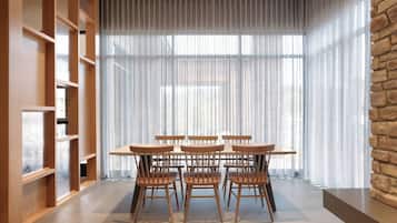 A dining area with a table and chairs, a wooden bookshelf, and a large window with sheer curtains.