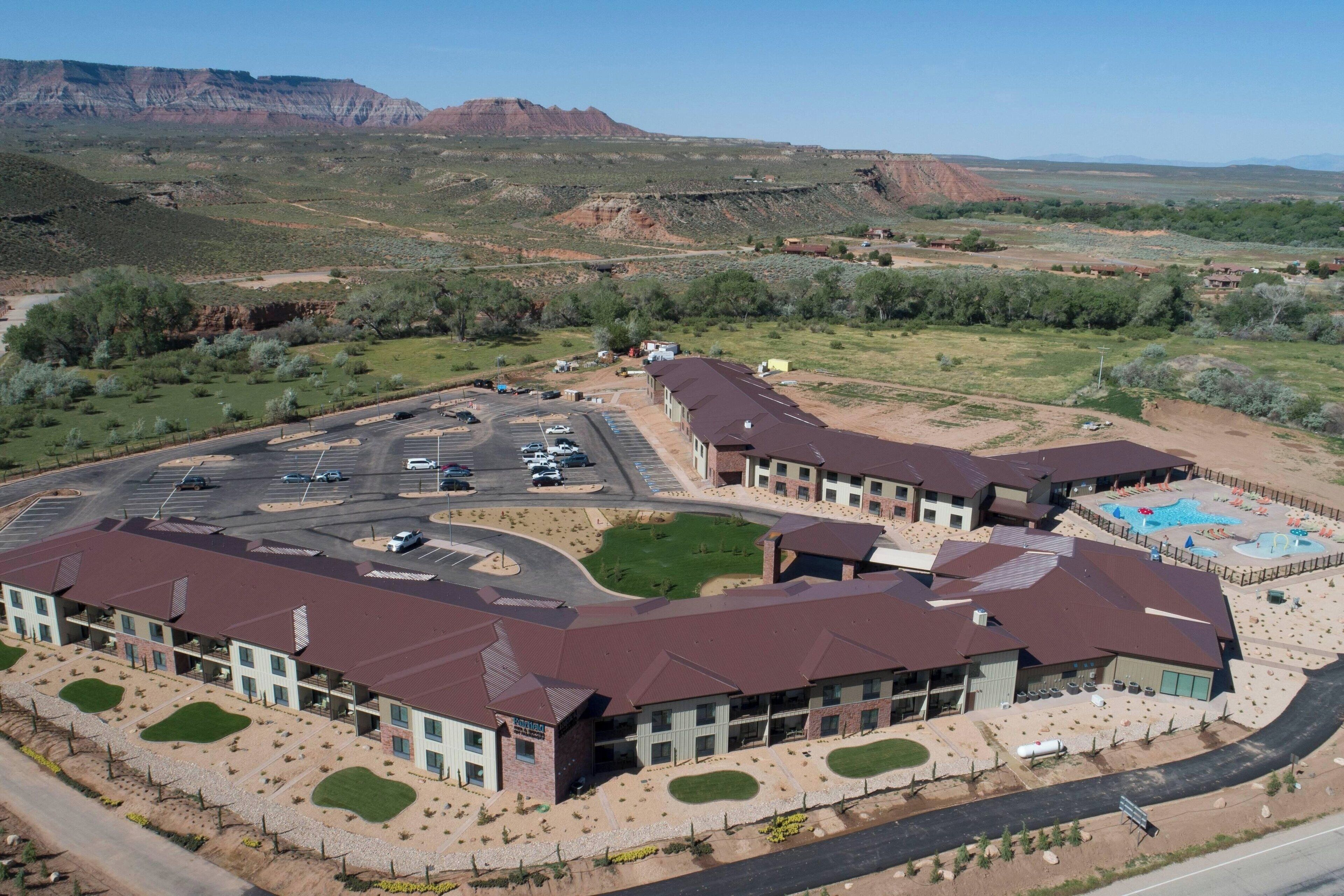 A large building with multiple sections, a parking lot, and a pool area.
