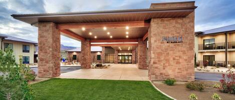 A hotel entrance with a covered walkway, brick pillars, and a well-maintained lawn.